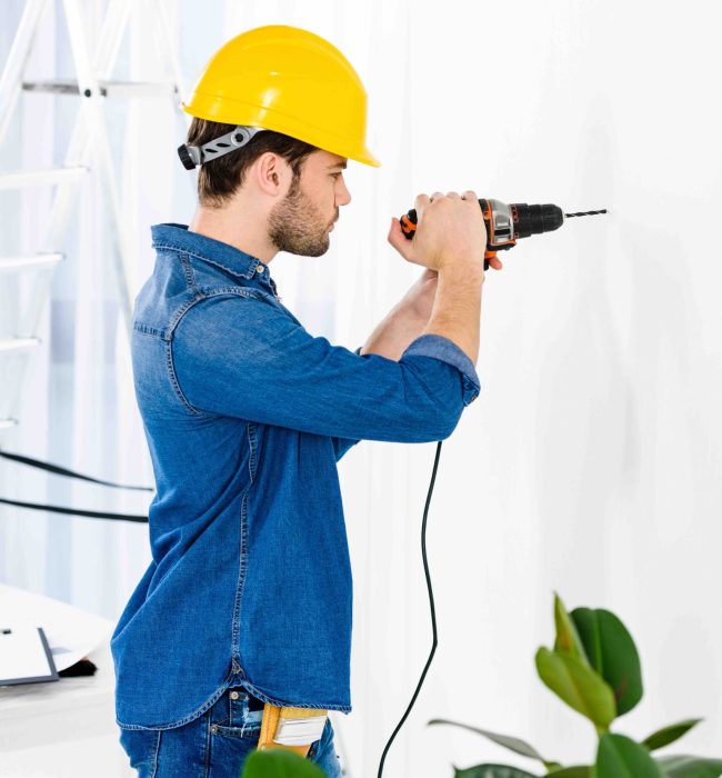 side view of handsome man using drill and making repairs side view of handsome man using drill and making repairs